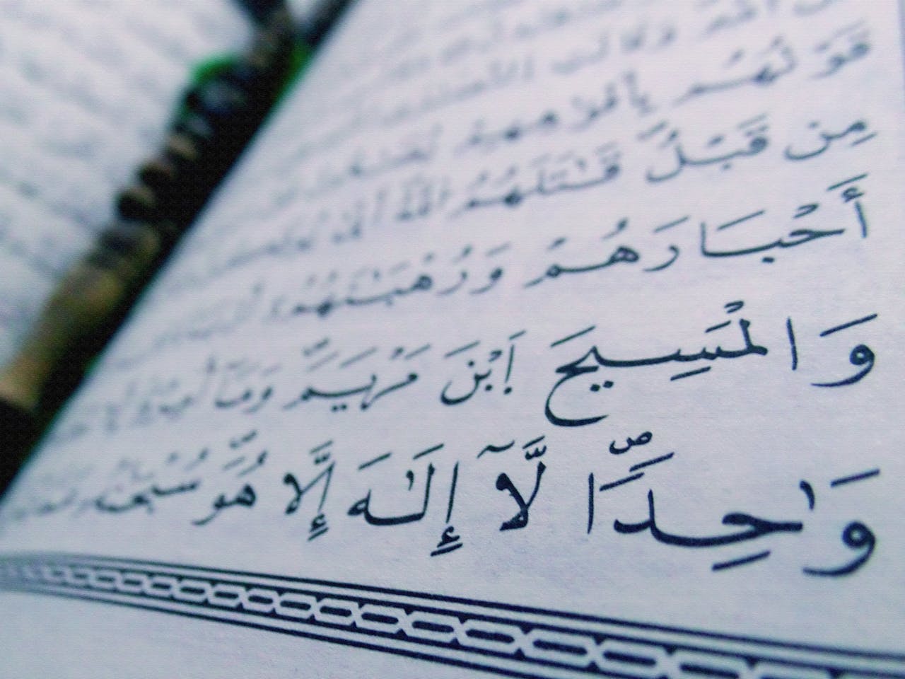 Detailed close-up of Arabic text with a pen resting on paper, focusing on intricate handwriting.